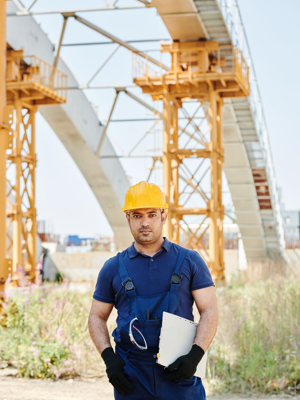 A site engineer with a clipboard in front of a bridge under construction