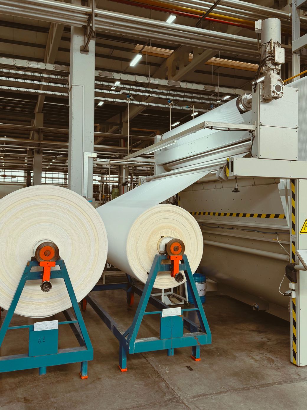 Rolls of greige cloth on A-frames beside a finishing range in a textile mill